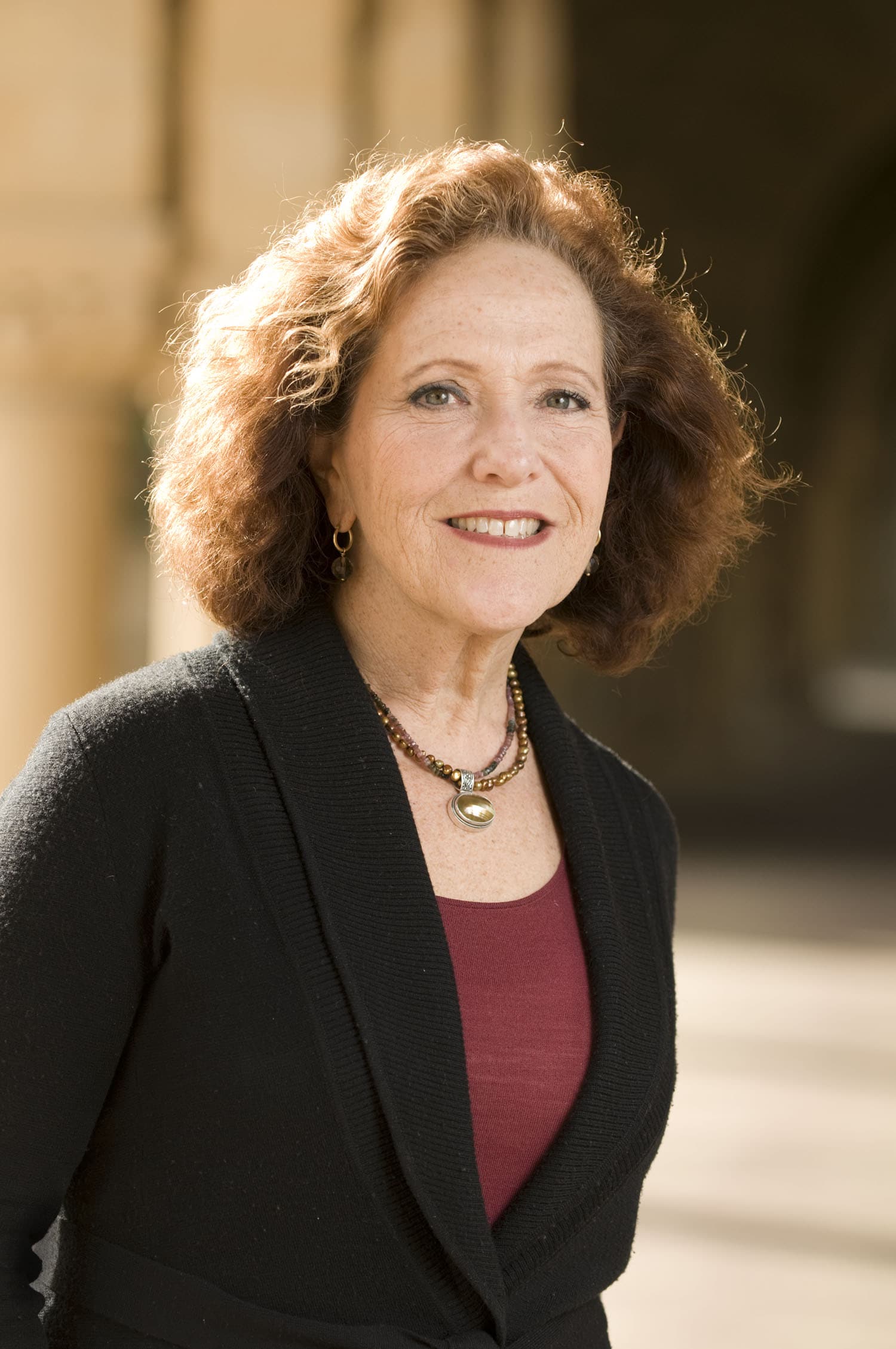 Portrait of a woman with auburn hair, wearing a black cardigan and maroon top.