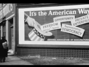 Black and white photo of a billboard promoting "The American Way" emphasizing freedom, opportunity, and private enterprise.
