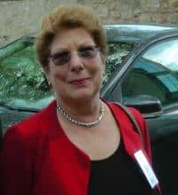 Headshot of a woman wearing a red jacket and glasses.