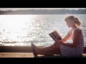 Woman relaxing by the lake, reading a book from her 2013 summer reading list.