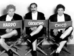 The Marx Brothers—Groucho, Harpo, and Chico—seated in director's chairs.