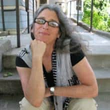 Woman with gray hair, seated on steps, contemplative expression.