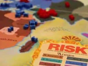Risk board game map with game pieces showing gameplay. "RISK" logo visible.