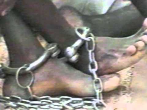 Close-up of shackled feet, a stark depiction of humanity violated.