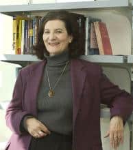 Portrait of a woman leaning against bookshelves.