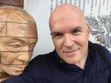 Man posing next to a carved wooden head.