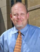 Portrait of a middle-aged man in a light blue shirt and orange tie.