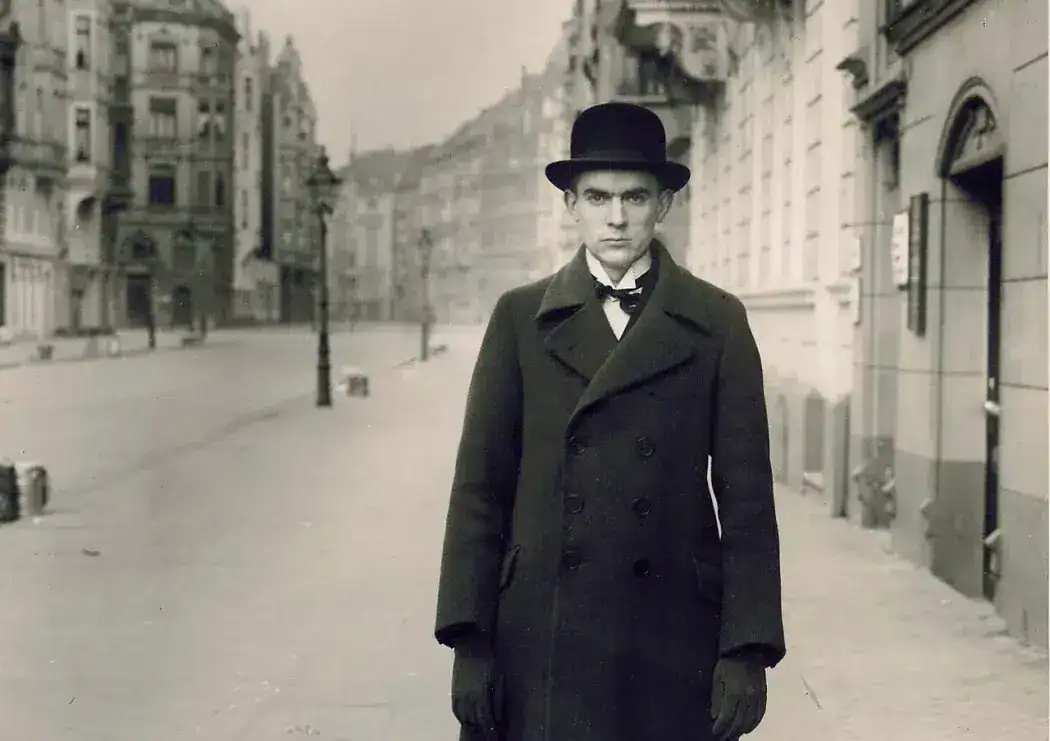 Robert Musil, Austrian author, in a bowler hat and overcoat on a city street.