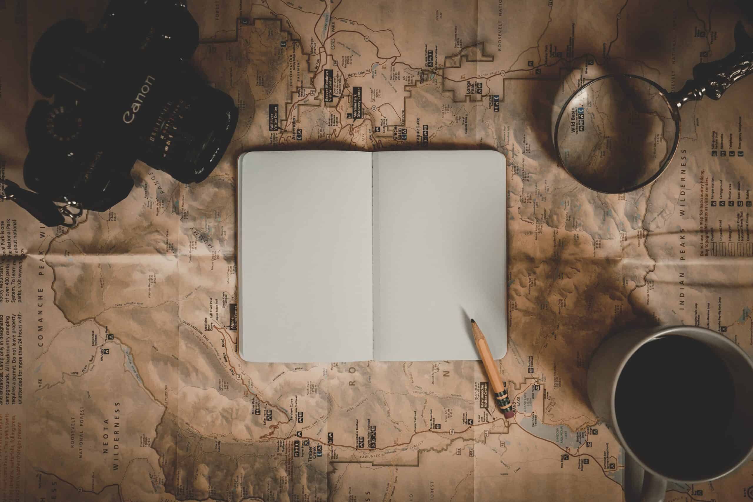 Map with blank notebook, pencil, camera, magnifying glass, and coffee. Planning a story or adventure.