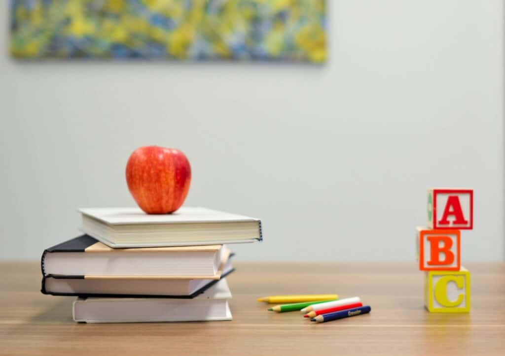 Stack of books with an apple, ABC blocks, and colored pencils on a desk