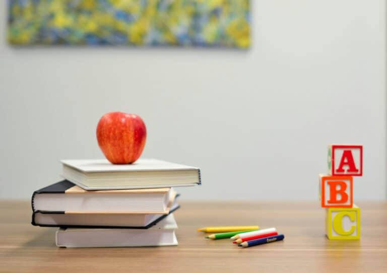Stack of books with an apple, ABC blocks, and colored pencils on a desk
