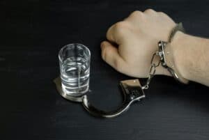 Hand in handcuffs attached to a shot glass of alcohol. Addiction concept.
