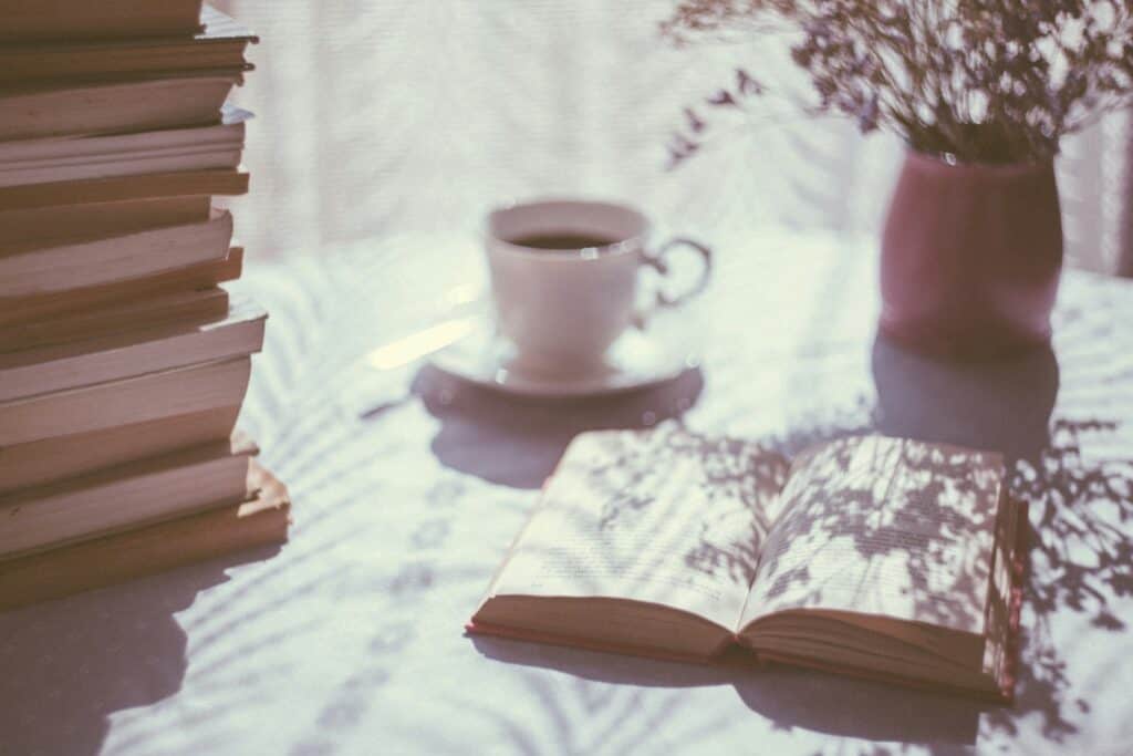 Stack of books, coffee, and flowers on a table, perfect for summer reading.