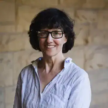 Smiling woman in glasses and a light blue shirt standing by a stone wall